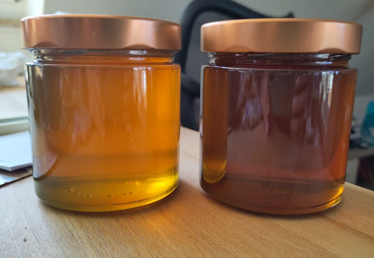 Zwei Honiggläser nebeneinander auf einem Holzbrett, links ein goldgelber, rechts ein rotbrauner Honig